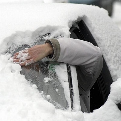 Мужчина чистит автомобиль рукой зимой